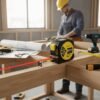 Digital Tape Measure In Use - Construction Work Construction worker using digital laser tape measure on wooden workbench with tools and blueprints