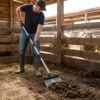 Heavy-Duty Scraper Shovel In Use Person using heavy-duty steel scraper shovel to clean barn floor with sheep in background